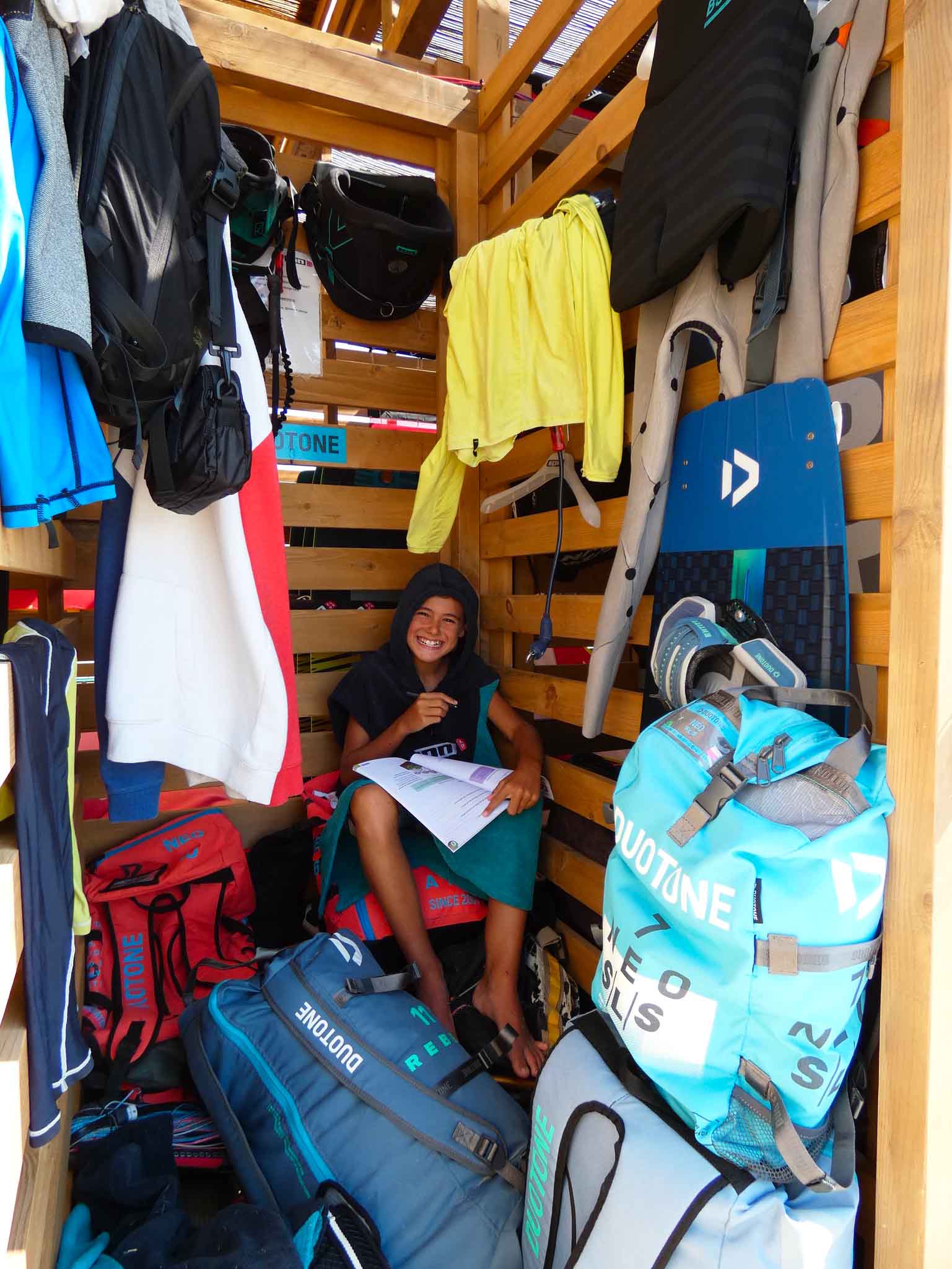 kids in a kitesurf storage doing his homework smiling