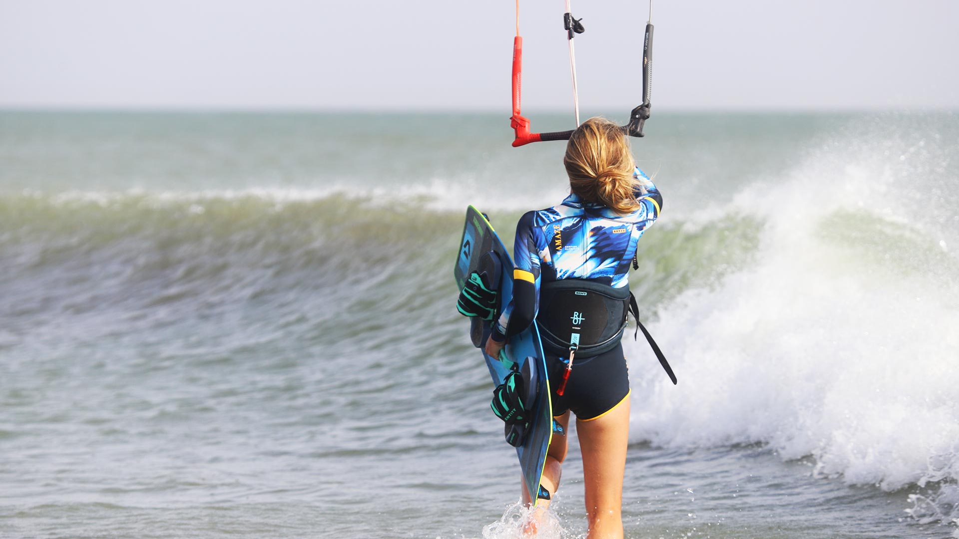 Jeune fille qui se mets à l'eau en kitesurf face à une vague