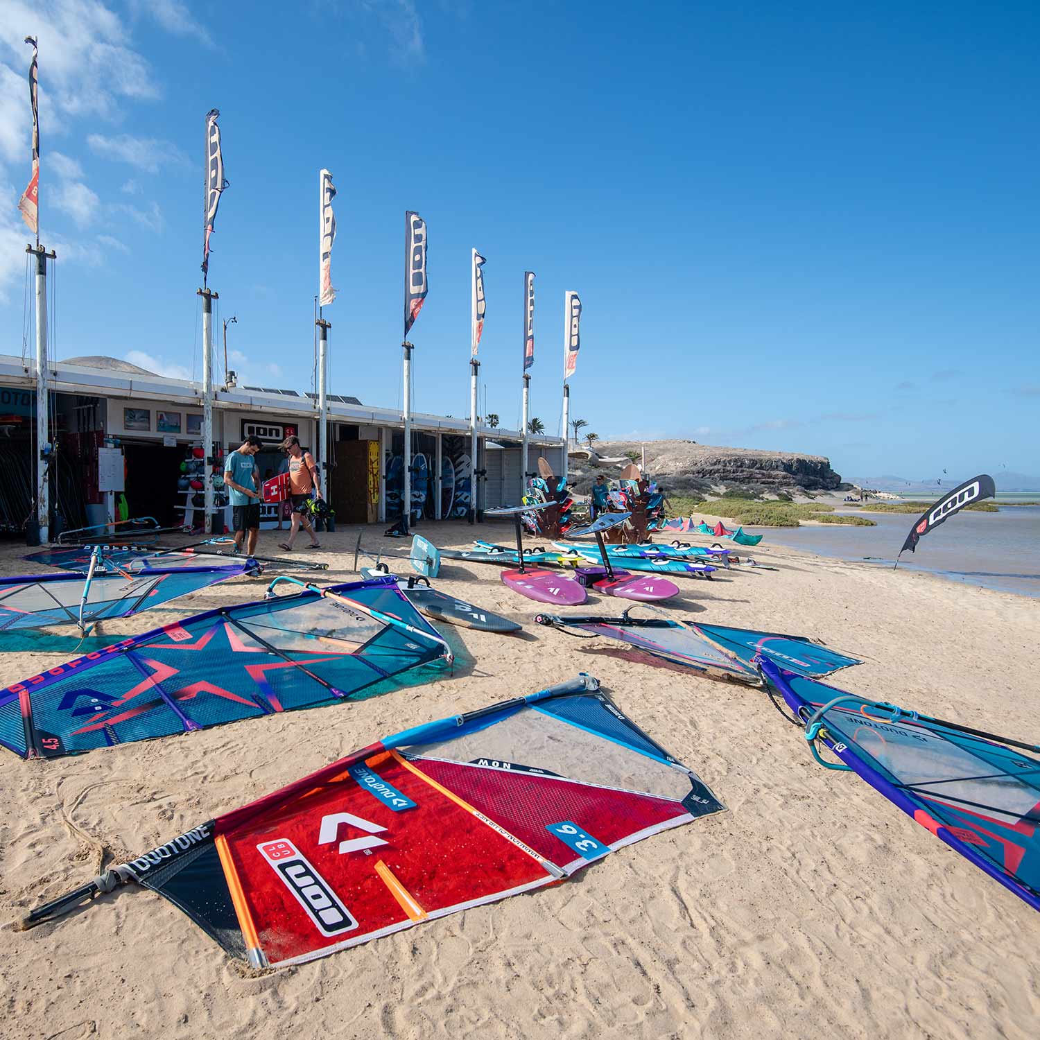 Voiles de windsurf posées sur le sol de sable blanc devant la réception du Ion Club Fuerteventura au spot de Risco del Paso. 