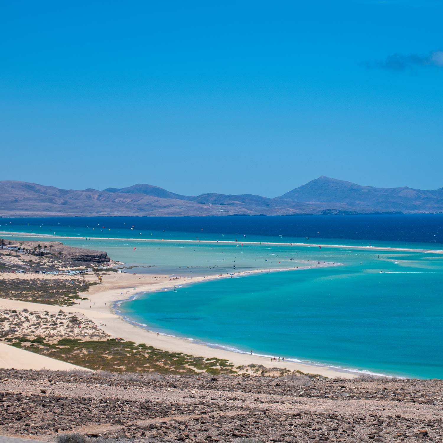 Spot-Risco-del-Paso-Ion-Club-Fuerteventura-The-Maui-of-Europe-2022.. Panoramisch uitzicht op het hele strand van Sotavento in Fuerteventura waar het kristalblauwe water lijkt op de blauwe kleur van de stranden van Maui in Hawaii.