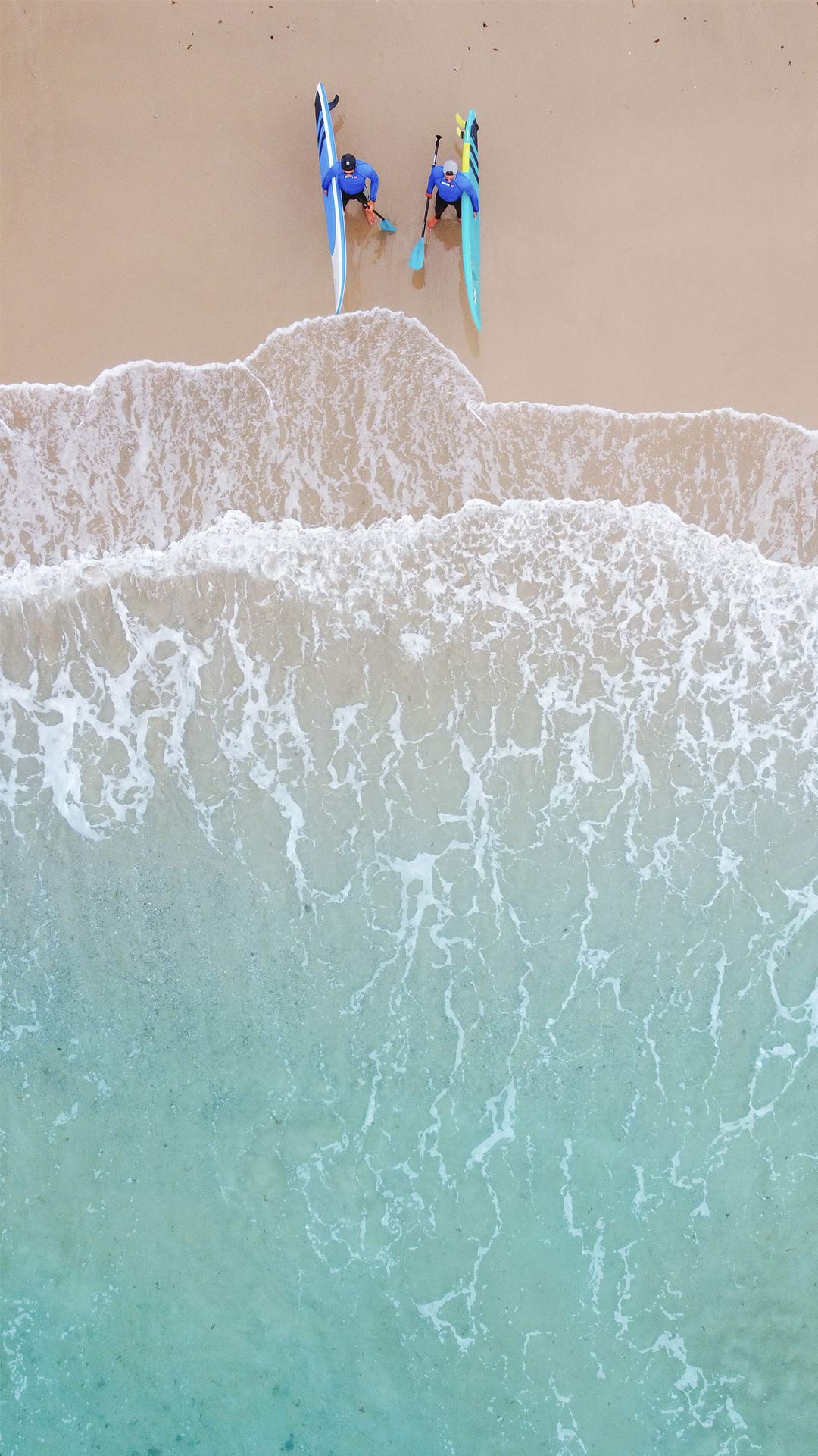 Luchtfoto van het strand van Tarifa waar twee leden van het Ion Club Tarifa team het peddelsurfmateriaal dragen waarmee ze het water ingaan om te genieten van een bijna Hawaiiaanse en ontspannen sfeer in vergelijking met Maui. 