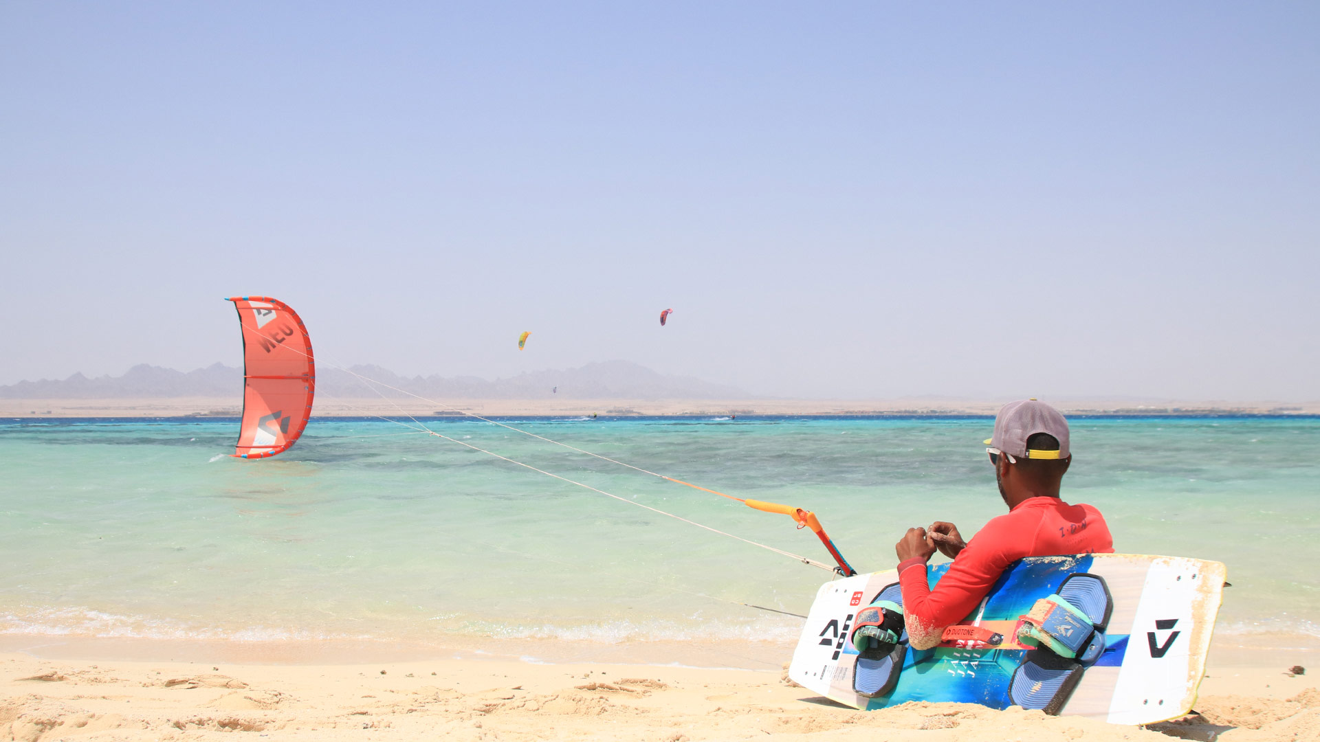 A kitesurfer, sitting on the sand leaning on his board waiting for the wind to lift his kite. sitt