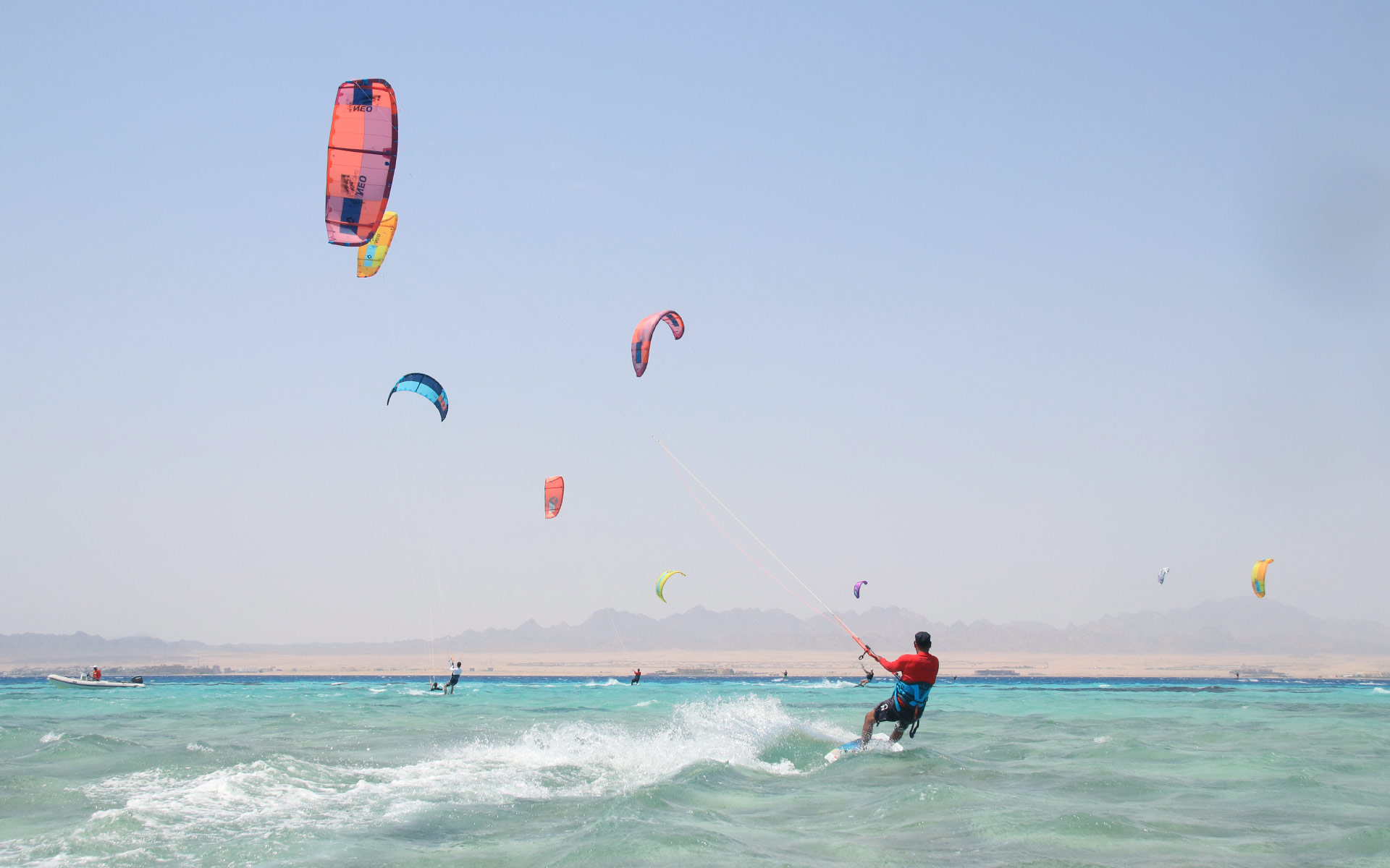 Blick auf die Skyline von Safaga, wo viele Drachen über den Himmel fliegen und Kitesurfer ihre Kitesurfing-Session genießen. 