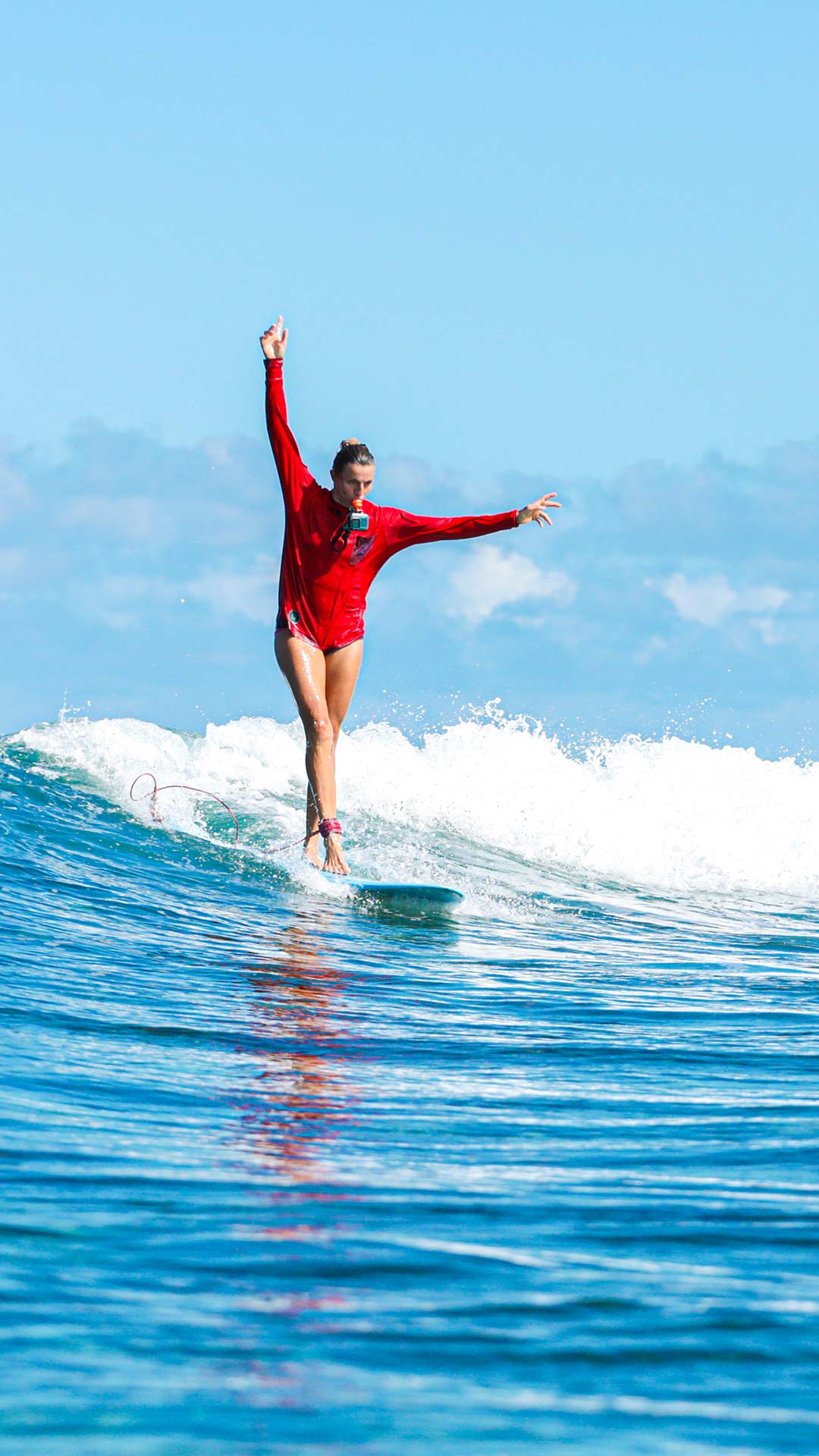 Eine Surflehrerin aus dem Ion Club-Team surft elegant auf einer Welle und nimmt ihren Ritt mit einer Go-Pro-Kamera auf, die an ihrem Mund hängt.