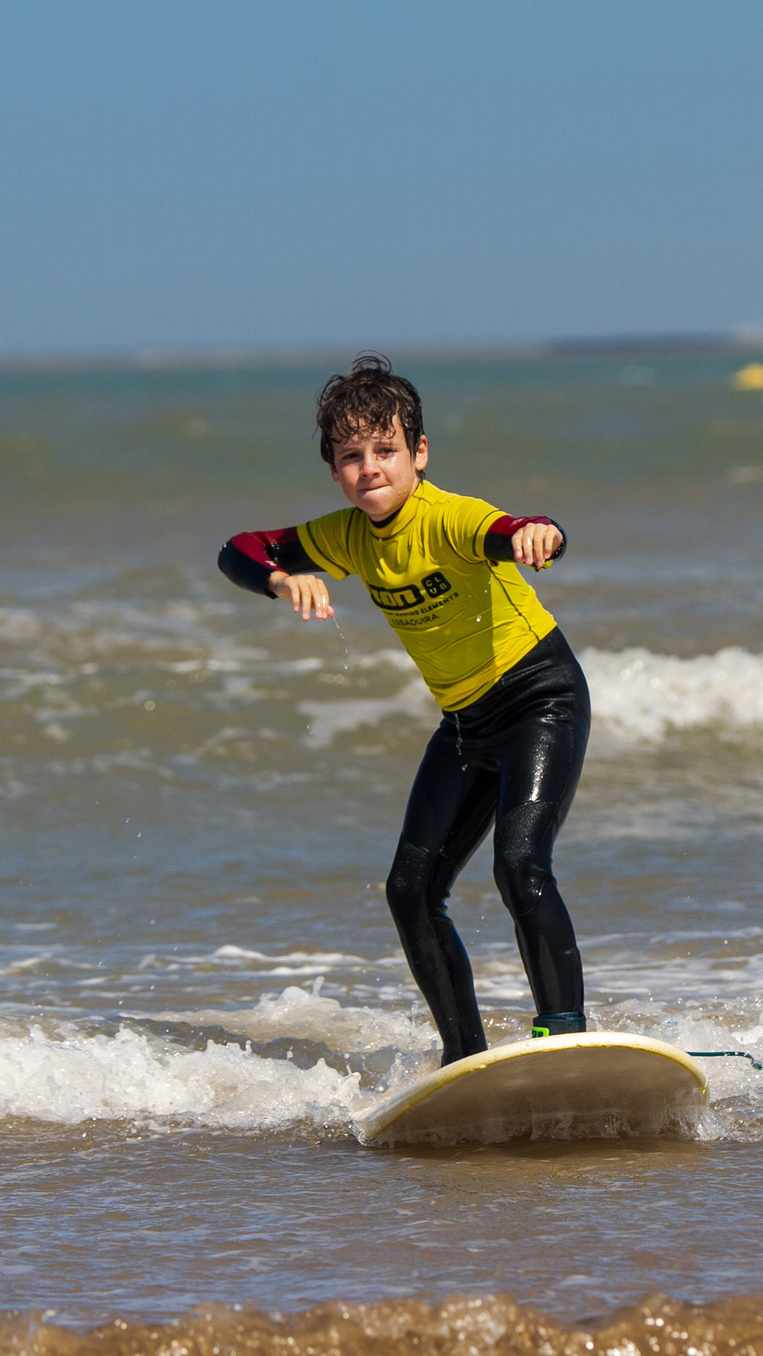A child surfing his first waves in one of his course with a proud look on his face.