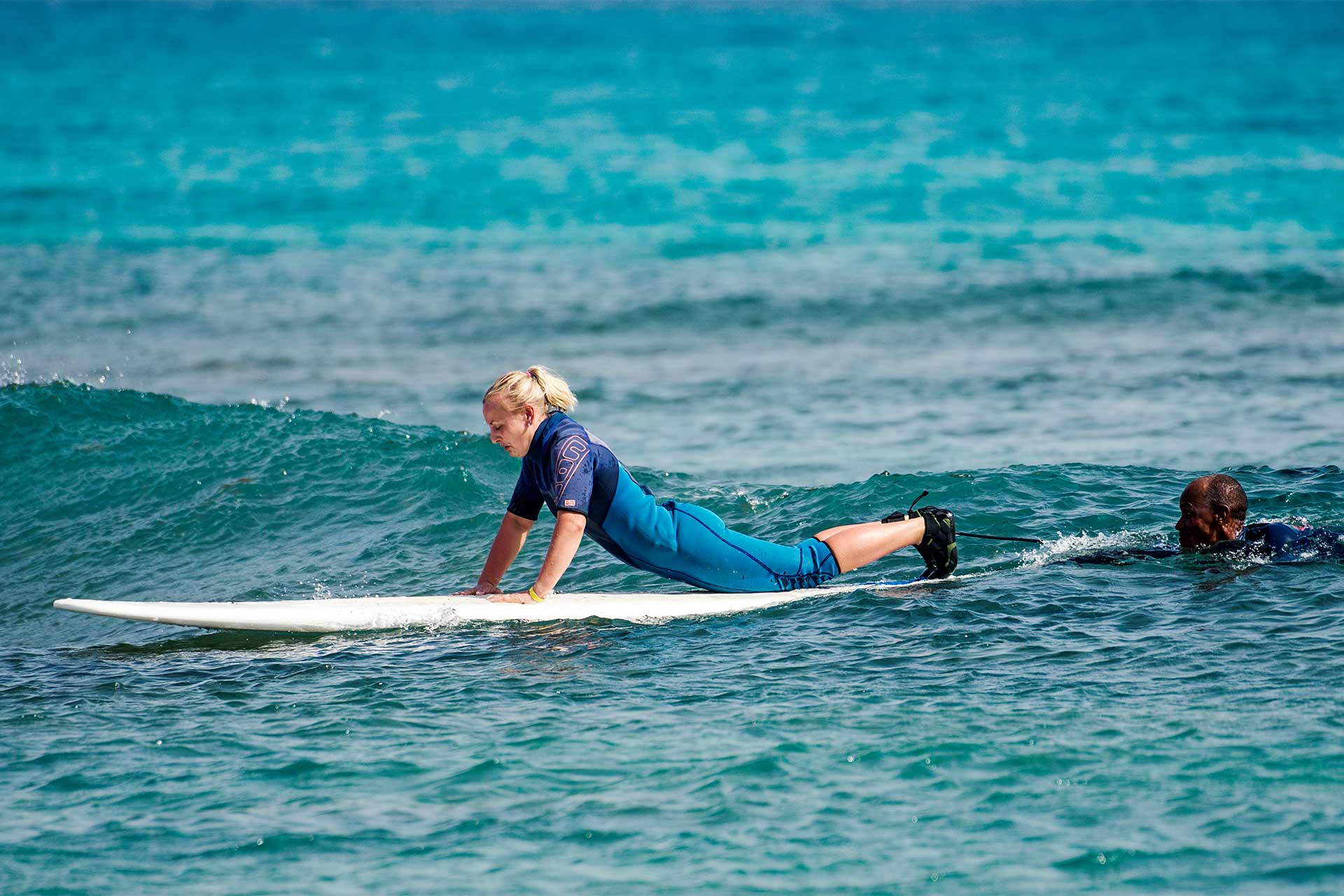 Une femme sur une planche de surf essaie d'attraper sa première vague avec son instructeur pendant un cours de surf dans l'eau. 