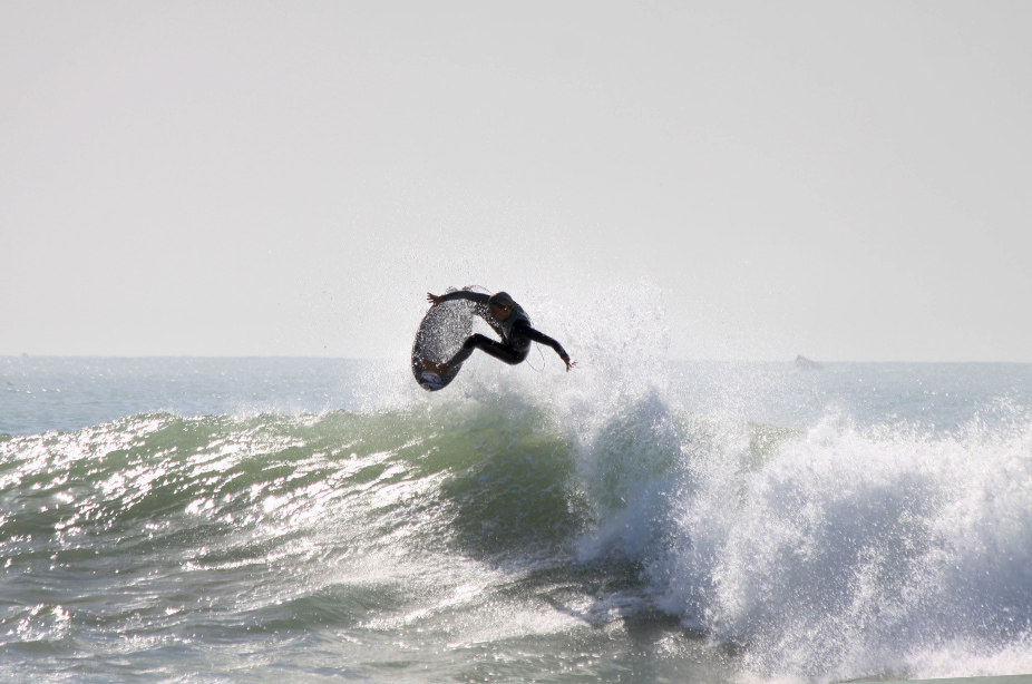 Un garçon surfe sur le haut de la vague en sautant et en faisant un tour avec sa planche pour démontrer ses talents de surfeur. 