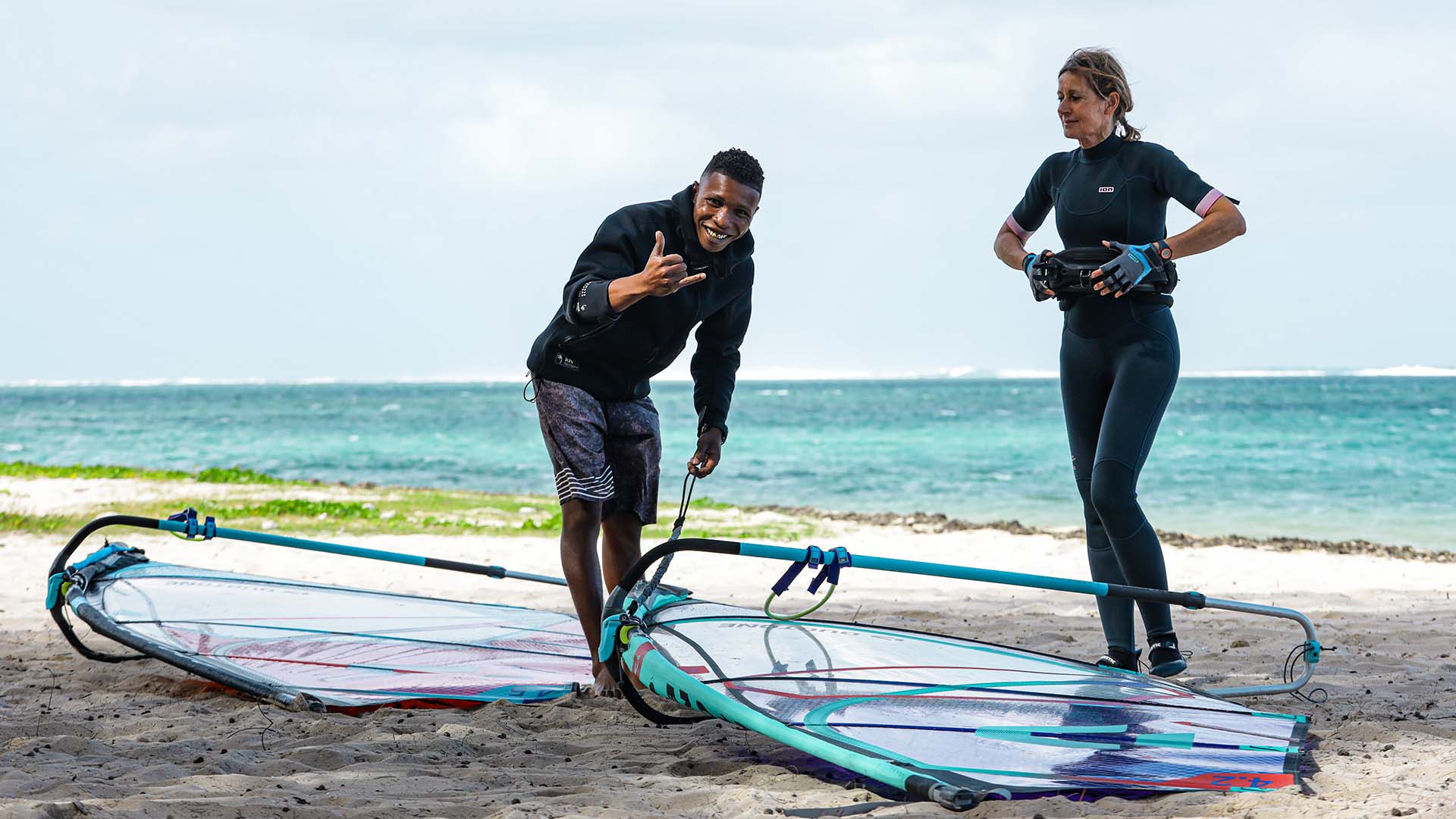 windsurf-lessons-start-with-ion-club-mauritius-13 Un instructor de kitefoil se prepara para navegar llevando la tabla de kitefoil con una mano y dirigiendo la cometa en el agua con la otra.